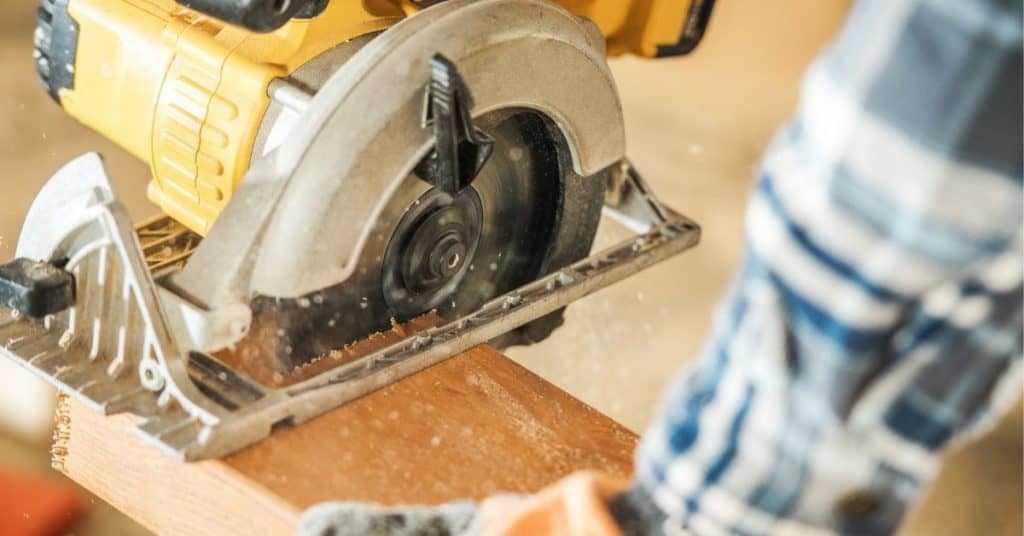 image is of a person holding the handle of a circular saw while the saw is cutting a piece of wood