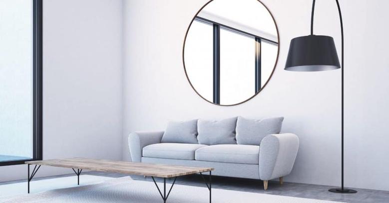 in this image there is a living room that has a sofa and a floor lamp above these items is a mirror that is facing a window. You can see the reflection of the window in the mirror by doing this small tweak a room will look much larger because the mirror will add depth