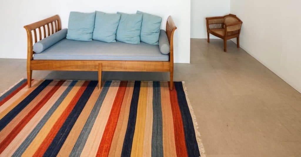 blue sofa with colorful striped rug under it making the room look longer with the rug.