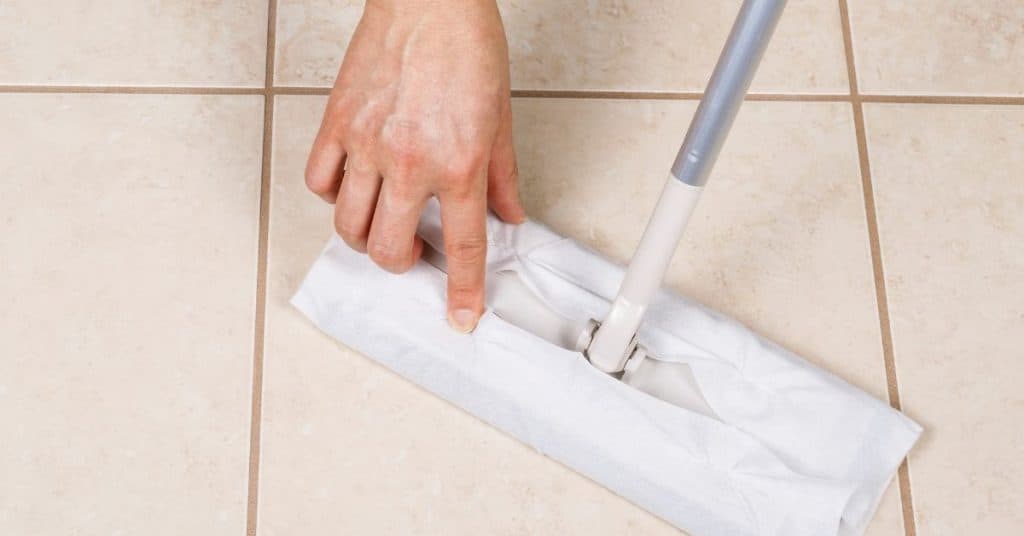 sweeping your bathroom tiles before mopping is the first step to getting your dirty floors ready to be cleaned. In this image we see a hand touching a swiffer to fix the swiffer towel that is attached to the swiffer broom