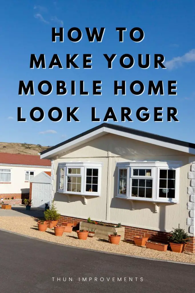 how to make your mobile home look larger shows a double wide mobile home with brick underneath with bay and garden windows with a side garage and a front wrapping of potted plants